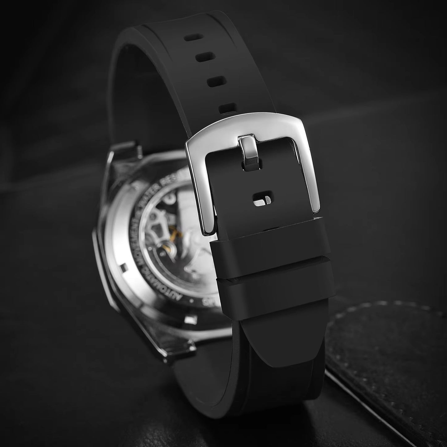 Close-up of a black watch strap with a metallic buckle on a dark background
