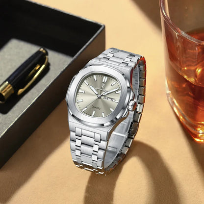Silver watch on a beige surface with a pen and glass of amber liquid in the background